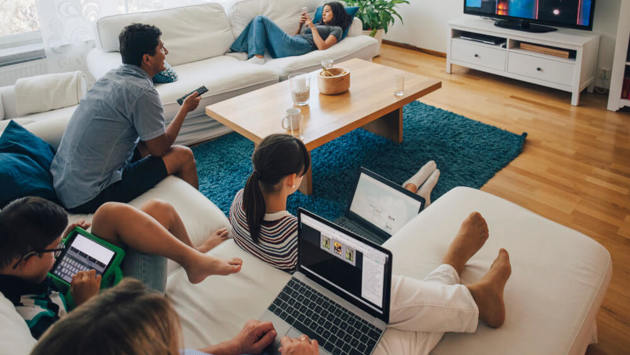 Blick von oben auf die Familie bei der Nutzung von Technologien, während sie sich im heimischen Wohnzimmer entspannt