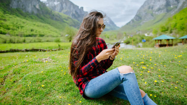 Ein Frau in den Bergen checkt auf ihrem Handy ihre Nachrichten.