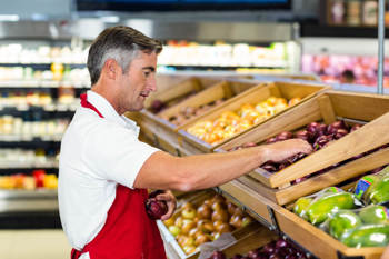 Ein Penny-Verkäufer drapiert frisches Obst auf der Verkaufsfläche im Laden.