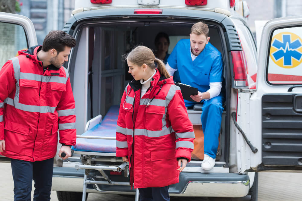 Zwei junge Rettungssanitäter heben eine Krankenliege aus einem Krankenwagen heraus.