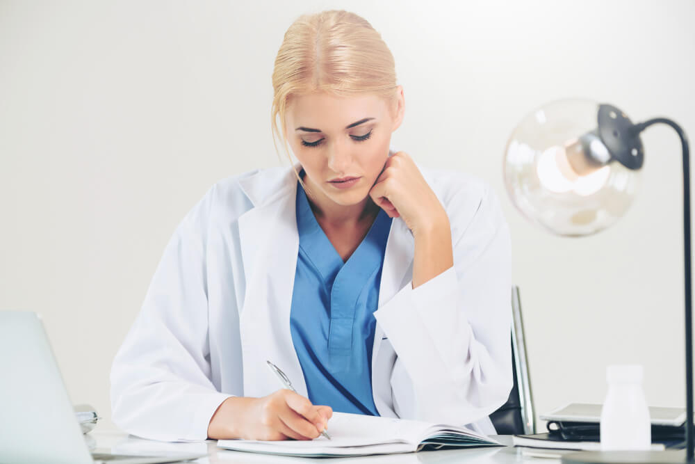 Eine junge Ärztin schreibt an ihrem Schreibtisch einen Bericht.