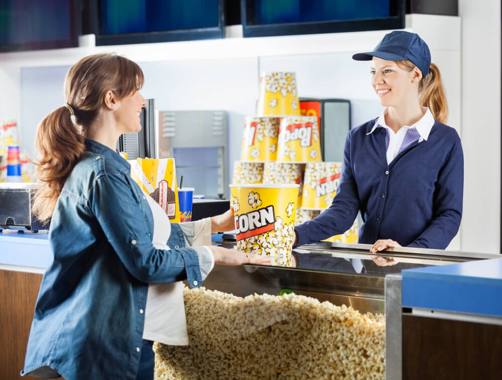 Frau kauft Popcorn bei einer Servicekraft am Kino-Konzessionsstand