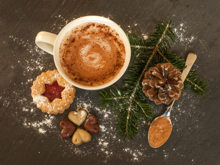 Kakao in einer weißen Kaffeetasse mit Weihnachtsplätzchen und einem Tannenzweig auf einem Holzuntergrund.