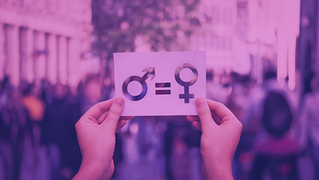 Hände halten ein Schild mit dem männlichen und weiblichen Geschlechtszeichen und einem Gleichheitszeichen vor einer Menschenmasse.