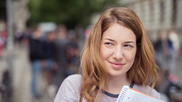Porträtfoto einer Schülerin mit einem Notizblock, die vor einer Menschenansammlung steht