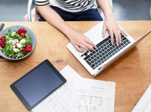 Frau am Schreibtisch mit Laptop neben einem Bauplan und Salat