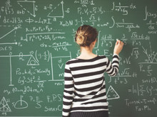 Schülerin schreibt mit Kreide mathematische Formeln an die Schultafel