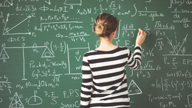 Schülerin schreibt mit Kreide mathematische Formeln an die Schultafel