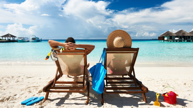 Zwei Urlauber liegen auf Strandliegen an einem türkisblauen Meer.