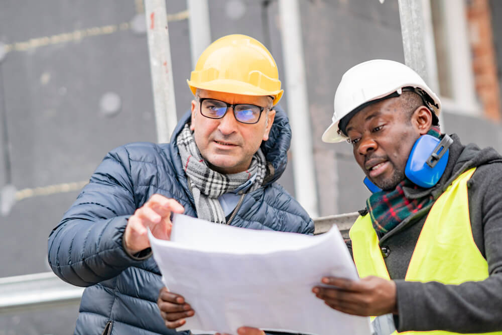 Zwei Männer betrachten auf der Baustelle gemeinsam einen Bauplan. 