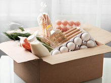 Pappkarton mit Eiern, Milch, Öl, Kräutern und anderen frischen Lebensmitteln.