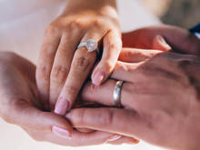 Eine Frauenhand mit Ehering liegt auf einer Männerhand mit Ehering.