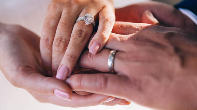Eine Frauenhand mit Ehering liegt auf einer Männerhand mit Ehering.