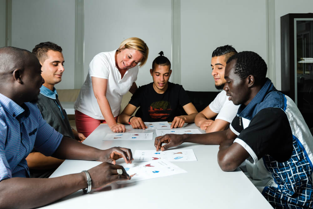 Eine Gruppe junger Flüchtlinge erlernt gemeinsam bei einem Sprachkurs die deutsche Sprache.