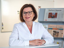 Marion Weckes, ehemalige Vergütungsexpertin der Hans-Böckler-Stiftung sitzt vor Zeitungen und lächelt.
