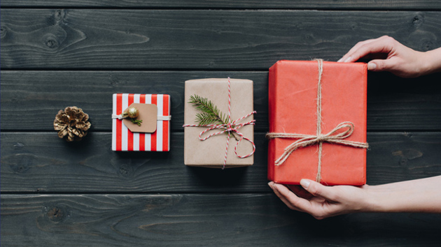 Drei der Größe nach aufgereihte Geschenke liegen auf einem Holzuntergrund und werden von Händen berührt.