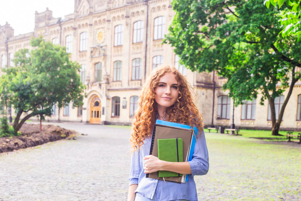 Eine junge Studentin steht vor einem Universitätsgebäude im Ausland.