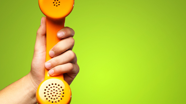 Eine Hand hält einen orangenen Telefonhörer vor einem grünen Hintergrund.