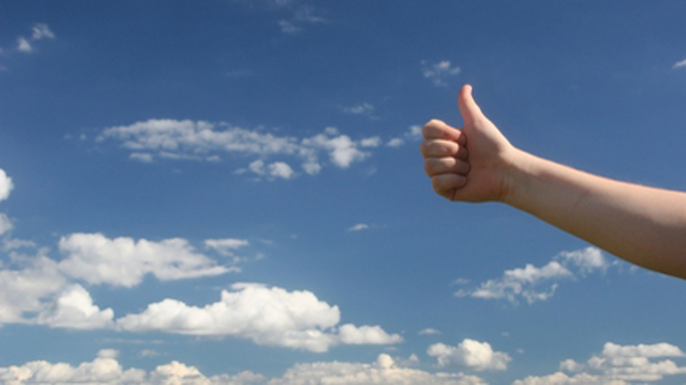 Eine Hand zeigt einen Daumen hoch vorm Himmel.