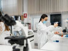 Wissenschaftlerin im weißen Kittel und mit Schutzmaske führt ein chemisches Experiment mit einer blauen Flüssigkeit in einem modernen Labor durch