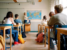 Eine Lehrerin deutet vor einer Klasse auf eine Landkarte auf Südamerika.