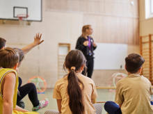 Sportlehrerin spricht mit ihrer Grundschulklasse in der Sporthalle