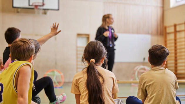 Sportlehrerin spricht mit ihrer Grundschulklasse in der Sporthalle