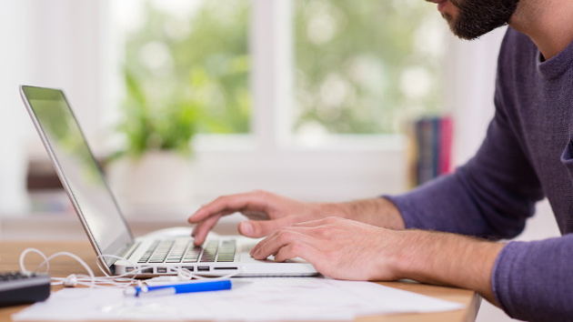 Ein Mann sitzt am Schreibtisch vor seinem Computer und schreibt auf der Tastatur.