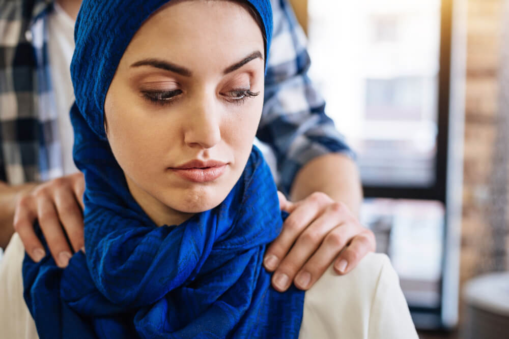 Sexuelle Belästigung am Arbeitsplatz: Muslimische Frau sitzt, während ein Mann sie belästigt.