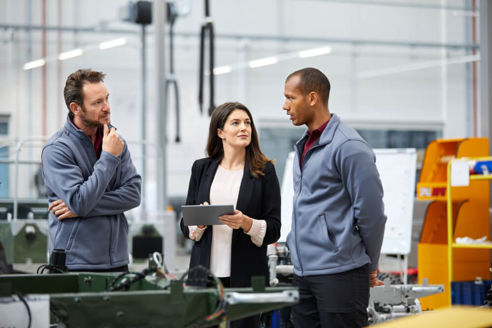 Fachkräfte stehen am Fließband der Autoproduktion. Autoingenieur diskutiert mit Kollegen in einer Autofabrik. 