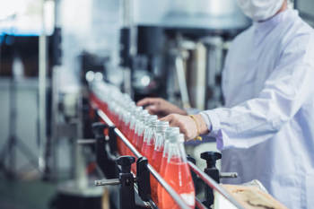 Nahaufname eines Hygienearbeiters, der in einer Getränkefabrik die abgefüllten Saft-Flaschen überprüft.