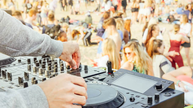 Hände eines DJs, der Musik gegen eine Menschenmenge am Strand mischt
